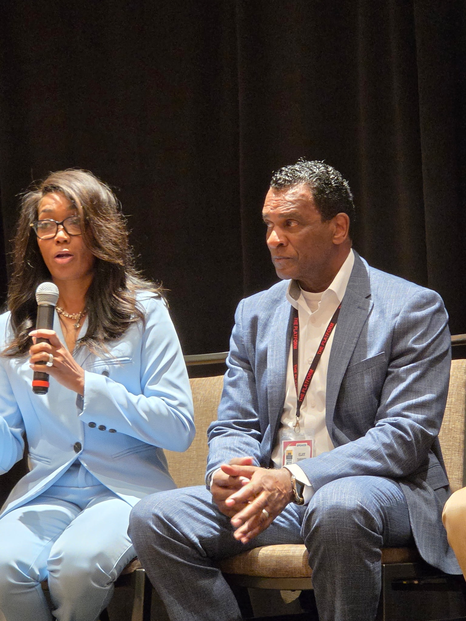 A woman speaking into a microphone seated beside a man during a Fearless and Focused, Inc. community panel.